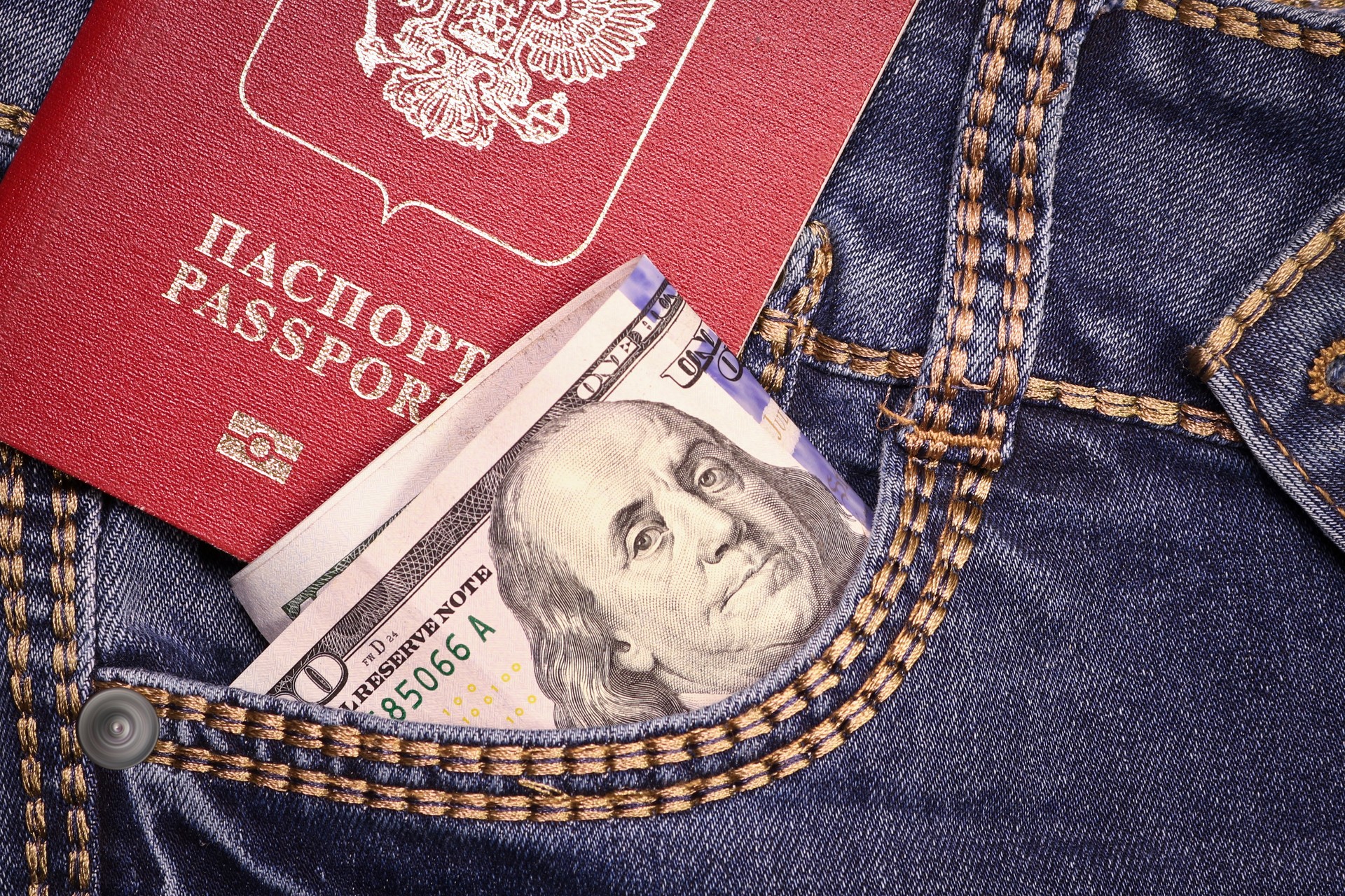 A stack of American hundred dollar bills in a pocket of blue jeans and an international passport of the Russian Federation. Money in your pocket, cash. Travel concept.